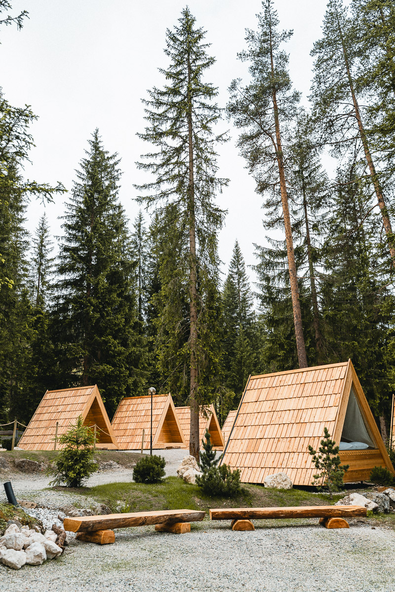 Timber A-frame glamping cabins among the trees at Camping Sass Dlacia
