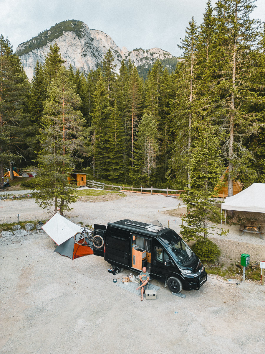 A camper van pitched among the pines with a bike on the back